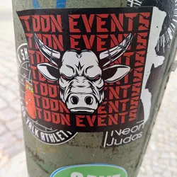 A sticker with the words "TOON EVENTS" repeated in red text on a black background.  The sticker features a graphic of a white bull's head with barbed wire horns in the center. The bull has angry red eyes. 