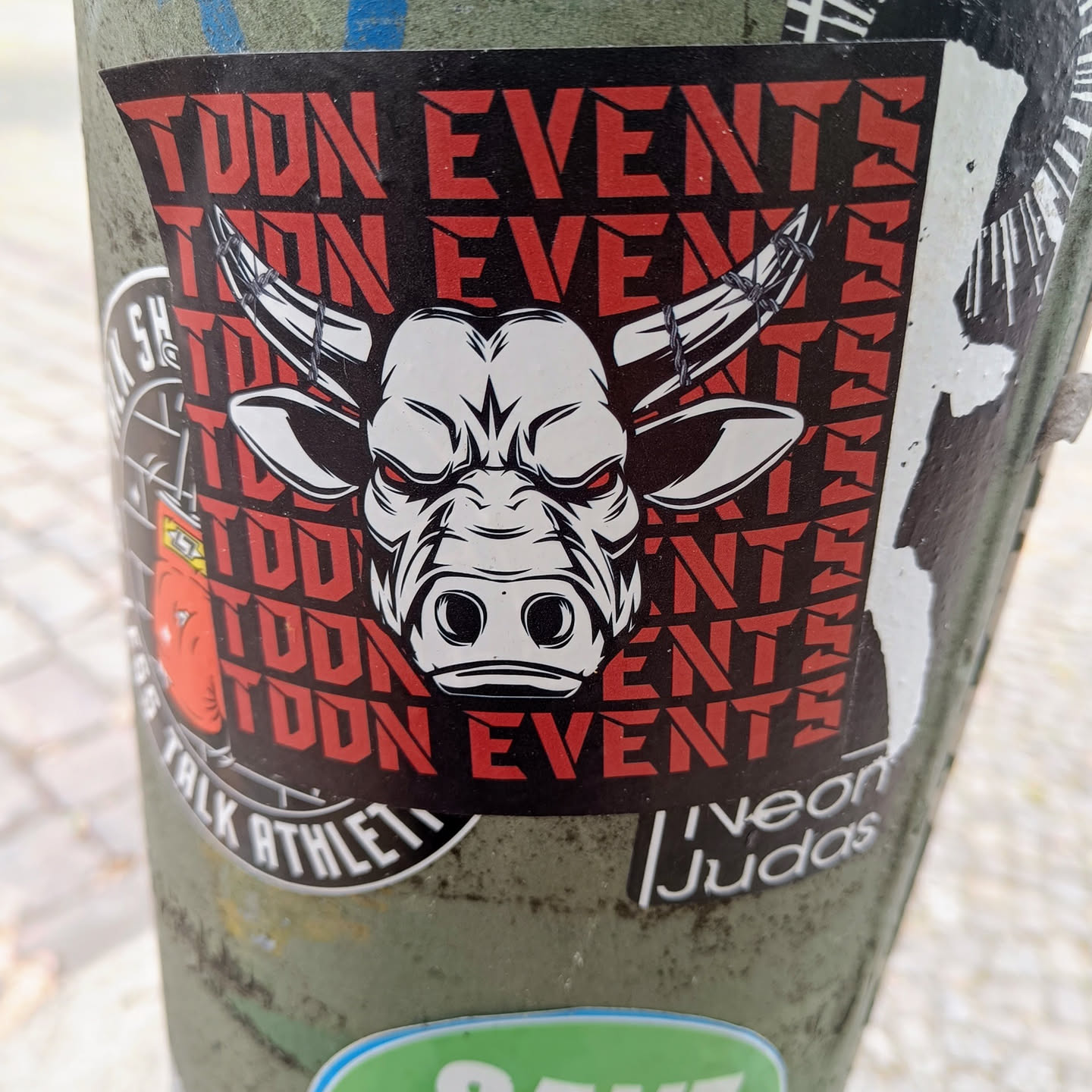 A sticker with the words "TOON EVENTS" repeated in red text on a black background.  The sticker features a graphic of a white bull's head with barbed wire horns in the center. The bull has angry red eyes. 