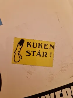 A yellow sticker with a drawing of a penis and the text "Kuken står!" which translates from Swedish to "The penis is standing!"