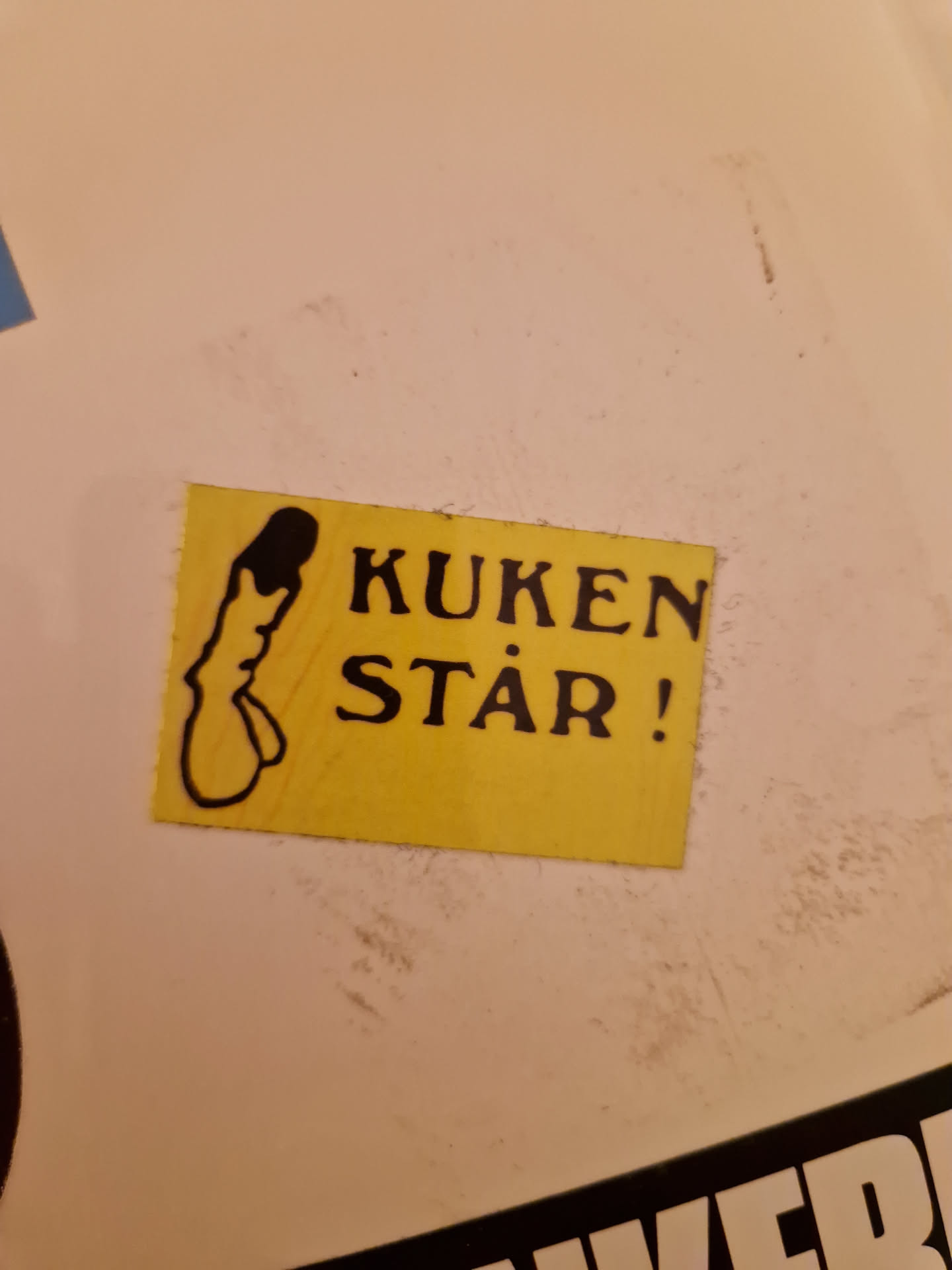 A yellow sticker with a drawing of a penis and the text "Kuken står!" which translates from Swedish to "The penis is standing!"