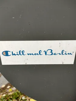 A sticker with the text "Chill mail Berlin" in a blue cursive font.  The left side of the text features a small Champion logo.