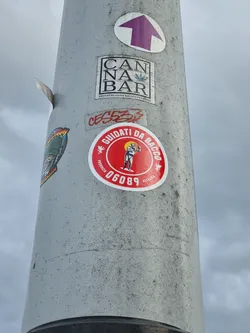 A red round sticker with a figure and text in Italian. The text translates to "Guided by Bacchus." It also has a number 06089.