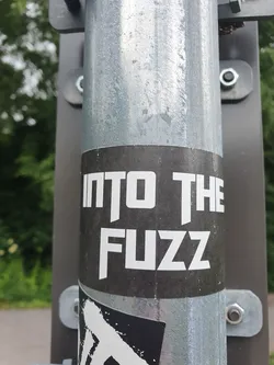 A black and white sticker on a metal pole with the text "INTO THE FUZZ" in a bold, sans-serif font.