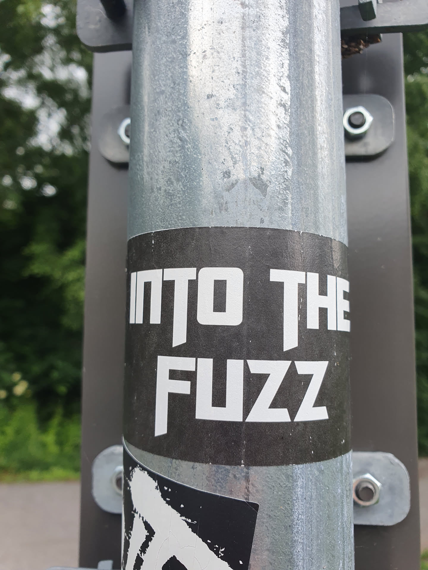 A black and white sticker on a metal pole with the text "INTO THE FUZZ" in a bold, sans-serif font.