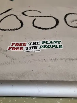 A sticker with the text "Free the plant, free the people" and a website address at the bottom. The text is in red and green on a white background.