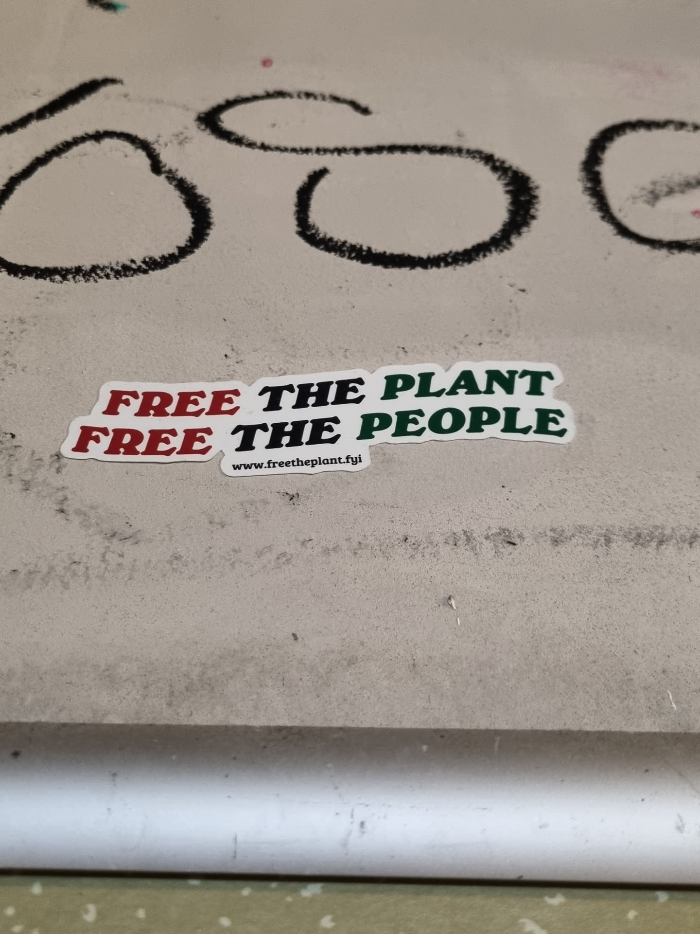A sticker with the text "Free the plant, free the people" and a website address at the bottom. The text is in red and green on a white background.