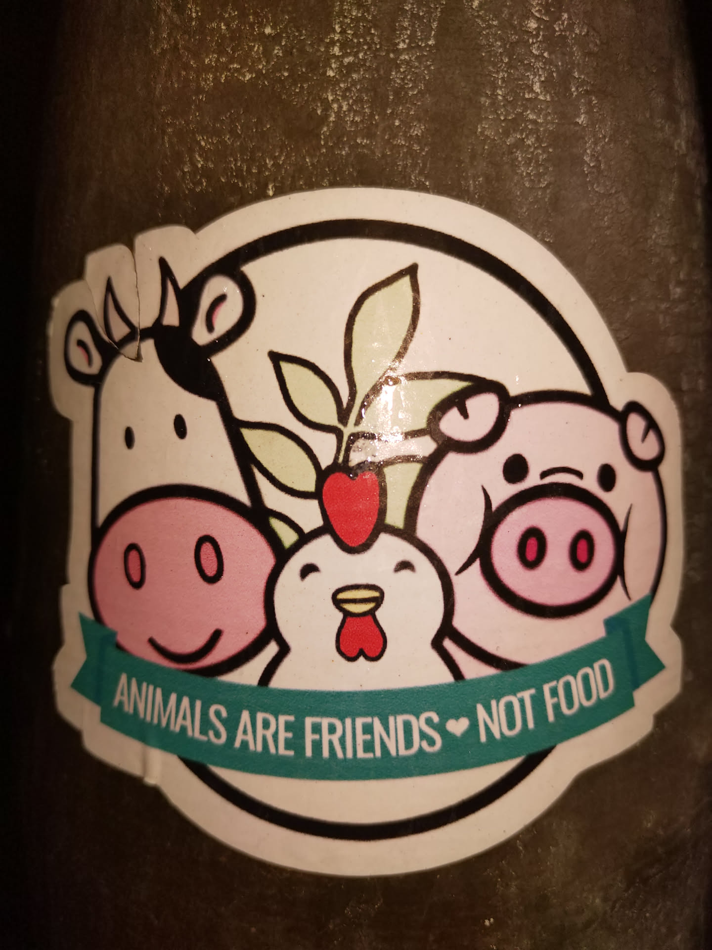 A sticker featuring a cow, pig, and chicken with a plant in the middle. The text on the sticker says, "Animals are friends ♥ not food."