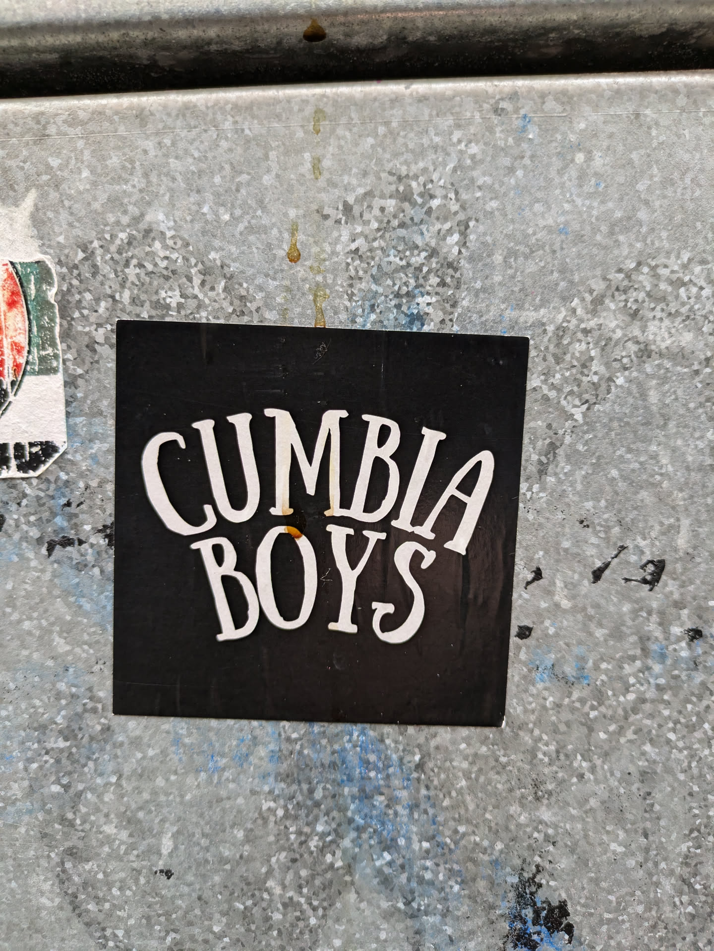 A black sticker with the text "Cumbia Boys" in white stylized lettering. The sticker is affixed to a weathered metal surface.