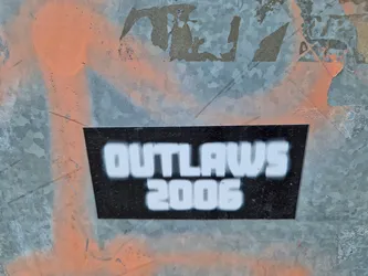 A black and white sticker with the text "OUTLAWS 2006" on it. The sticker is affixed to a metallic surface with some paint splatters on it.
