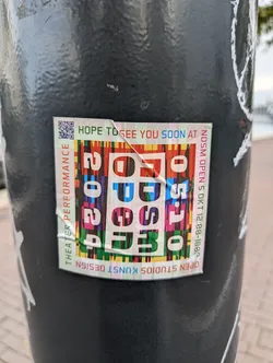 A colorful sticker promoting the NDSM Open Studios Kunst Design event, featuring a QR code and event details. The sticker has a unique design with a vibrant color palette and playful typography. The event takes place on October 5th from 12:00 to 18:00. 