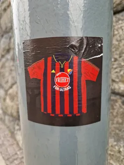 Sticker featuring a stylized football jersey with vertical stripes, a logo, and the text "FRIHET FOR ULTRAS". The sticker is attached to a pole outdoors.