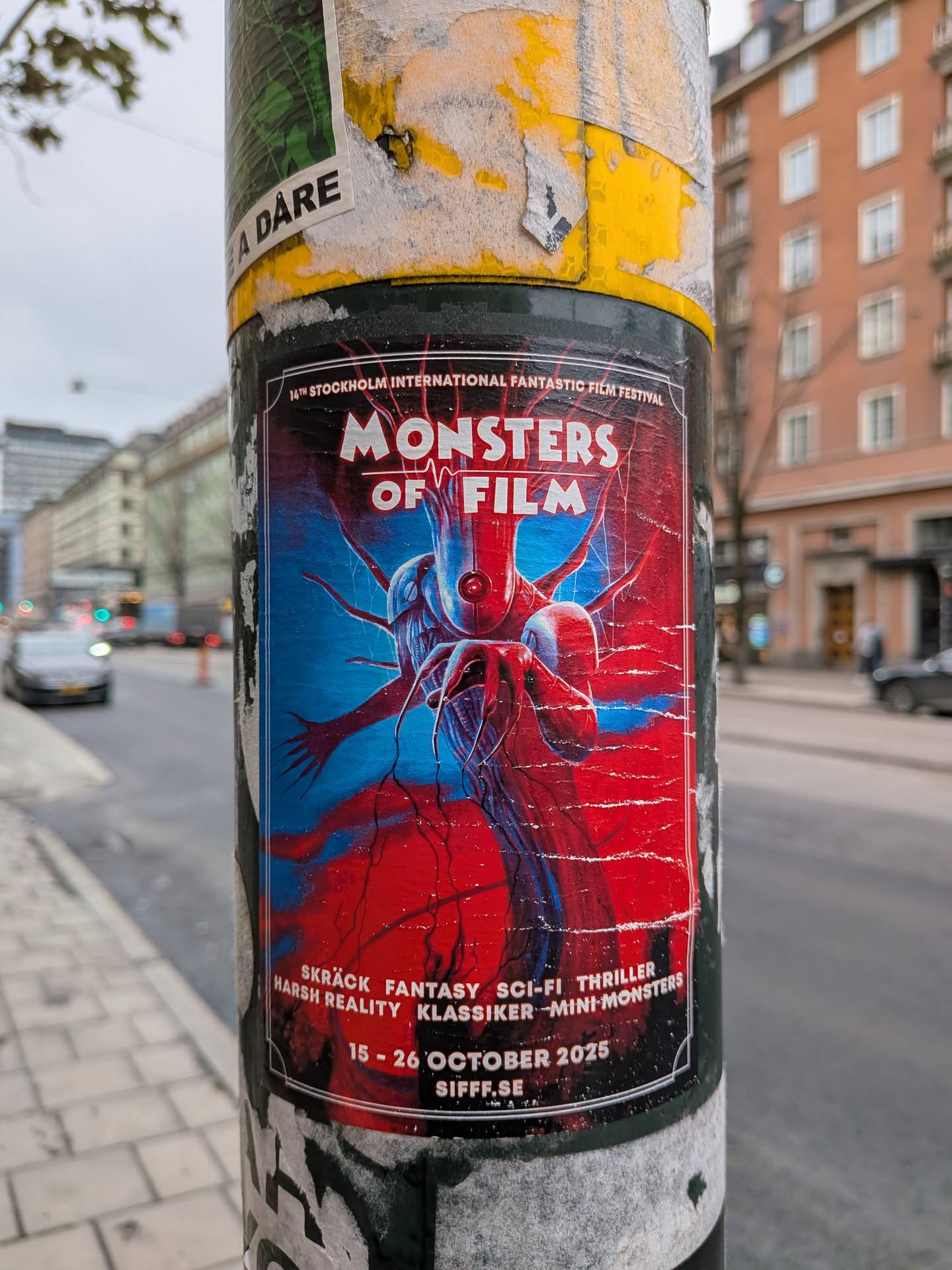 The sticker is a poster for the 'Monsters of Film' event, part of the 14th Stockholm International Fantastic Film Festival. It features a striking, abstract illustration of a creature with multiple tentacles and a central eye-like feature, rendered in vibrant blues and reds. The background is a chaotic blend of these colors, suggesting a dynamic and possibly unsettling theme. The text is in white and is arranged in a structured manner, with the festival name and dates clearly visible. The overall aesthetic is bold and eye-catching, typical of promotional material for a genre film festival.