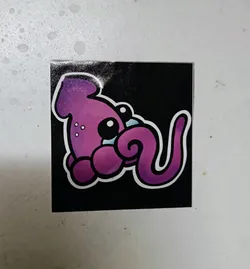 A cute purple squid with big eyes and a curled tentacle. The sticker has a black background and is printed with high quality.