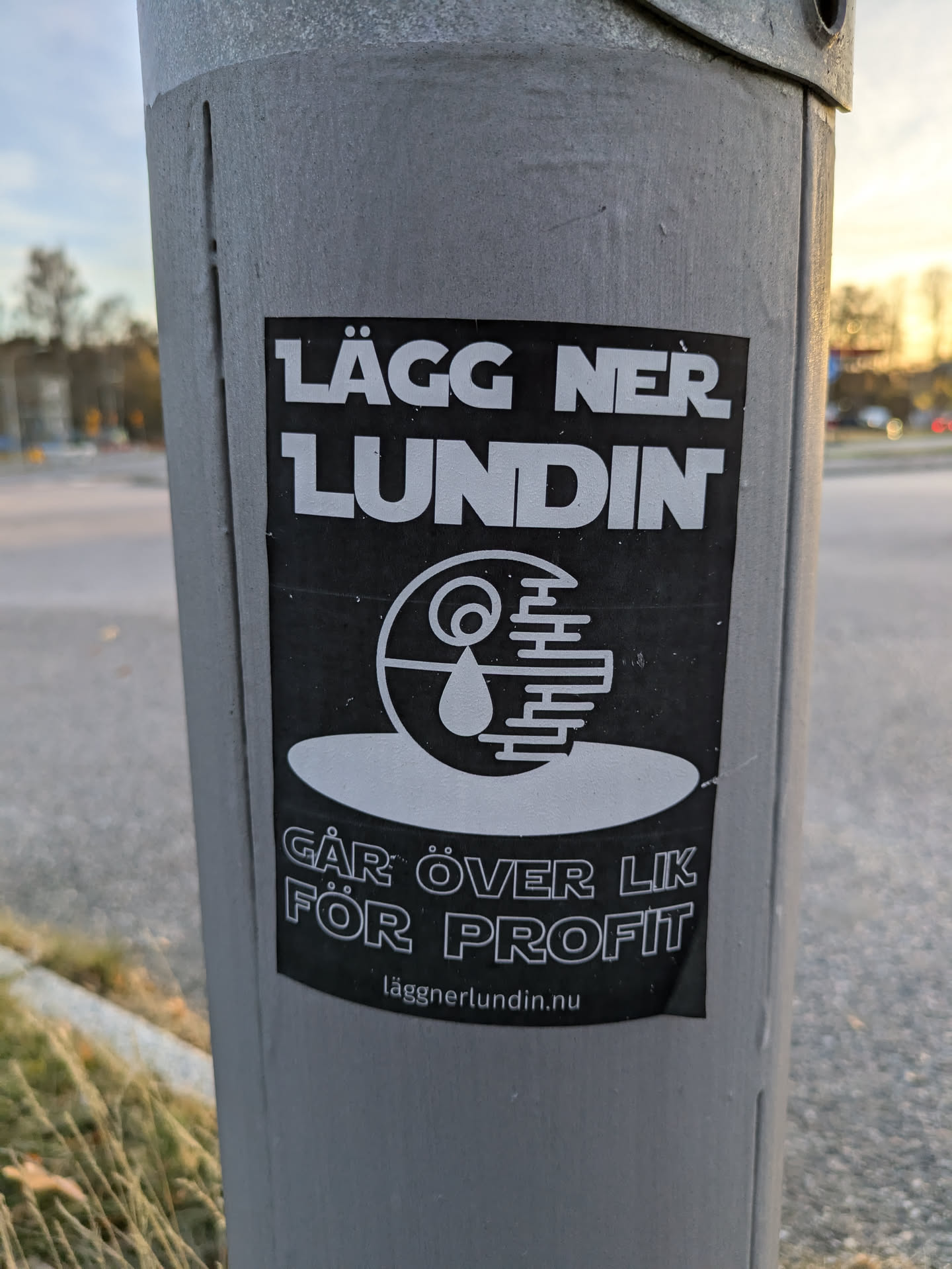 A black and white sticker with a design resembling the Death Star with a drop of blood in the center. The text on the sticker says "Lägg ner Lundin" (Shut down Lundin) and "Går över lik för profit" (Walks over corpses for profit) in Swedish. There is also a website address at the bottom: laggnerlundin.nu.