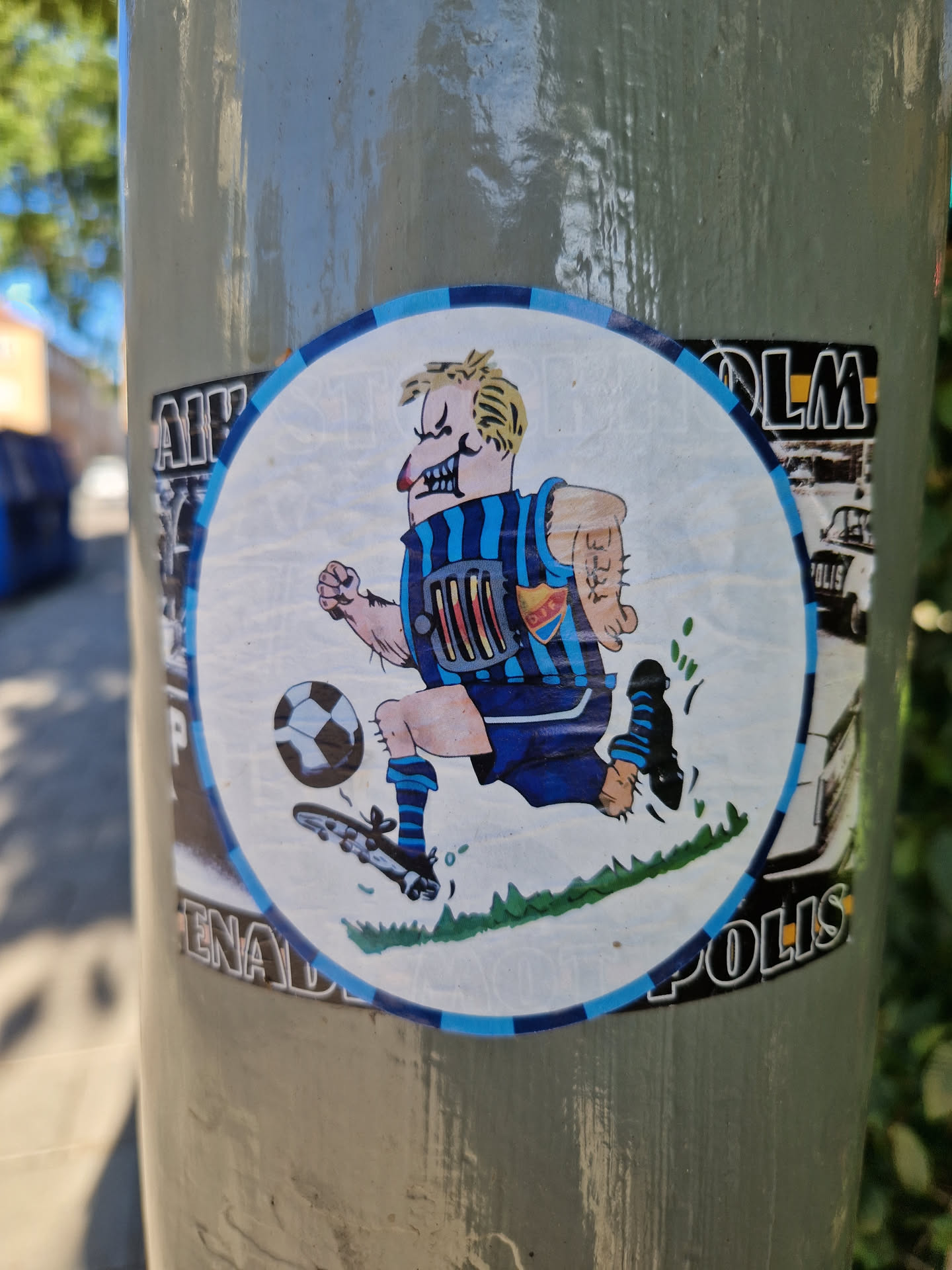 A round sticker featuring a cartoon illustration of a soccer player in blue and white uniform running with a ball. The style is reminiscent of comic strips. 