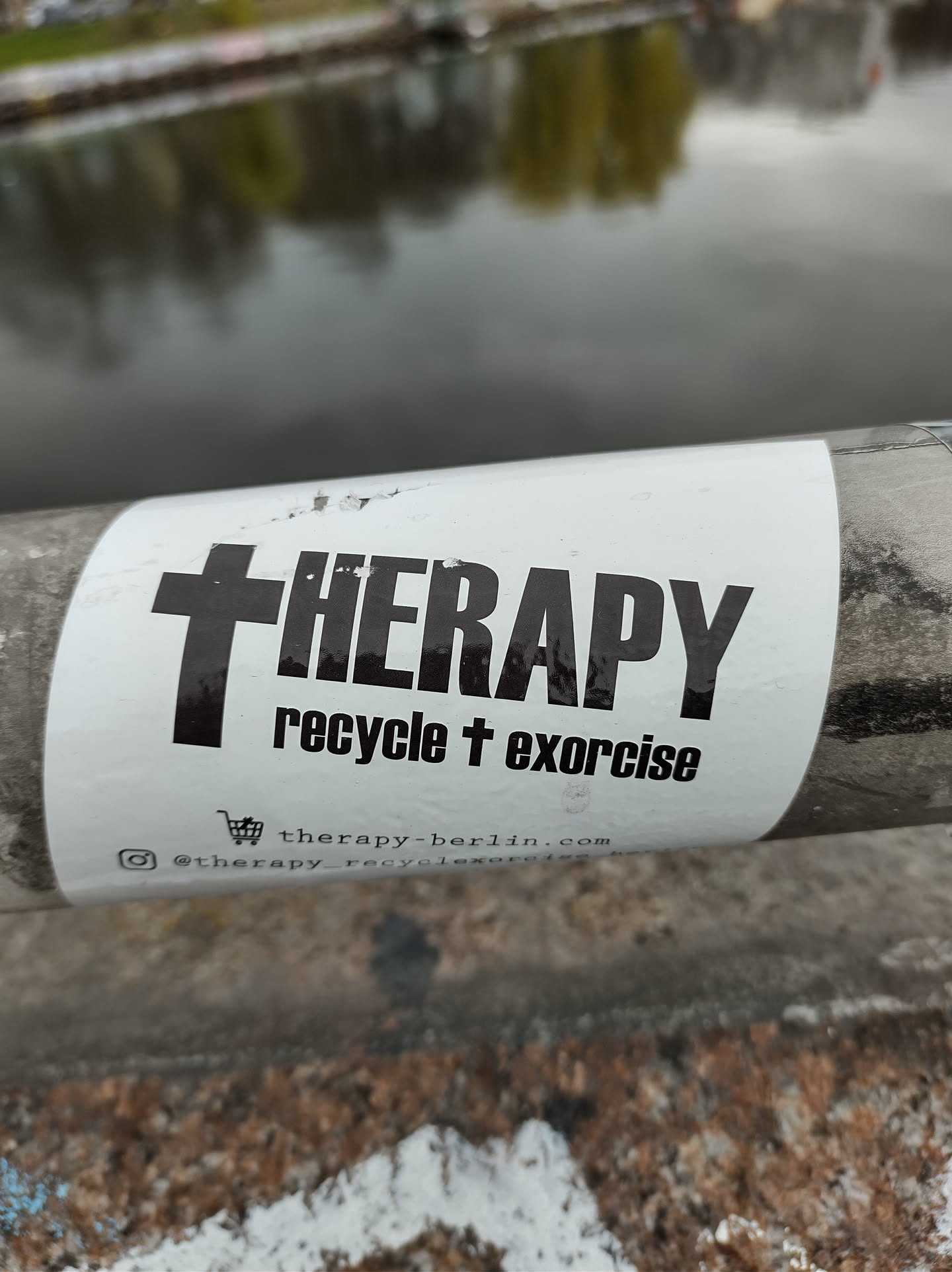 A sticker with a cross and the word THERAPY. Below it says 'recycle + exorcise'. It includes a website and Instagram account.