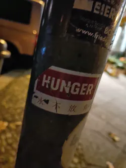 A sticker on a pole with the word HUNGER in large letters. There is also some Chinese text underneath.