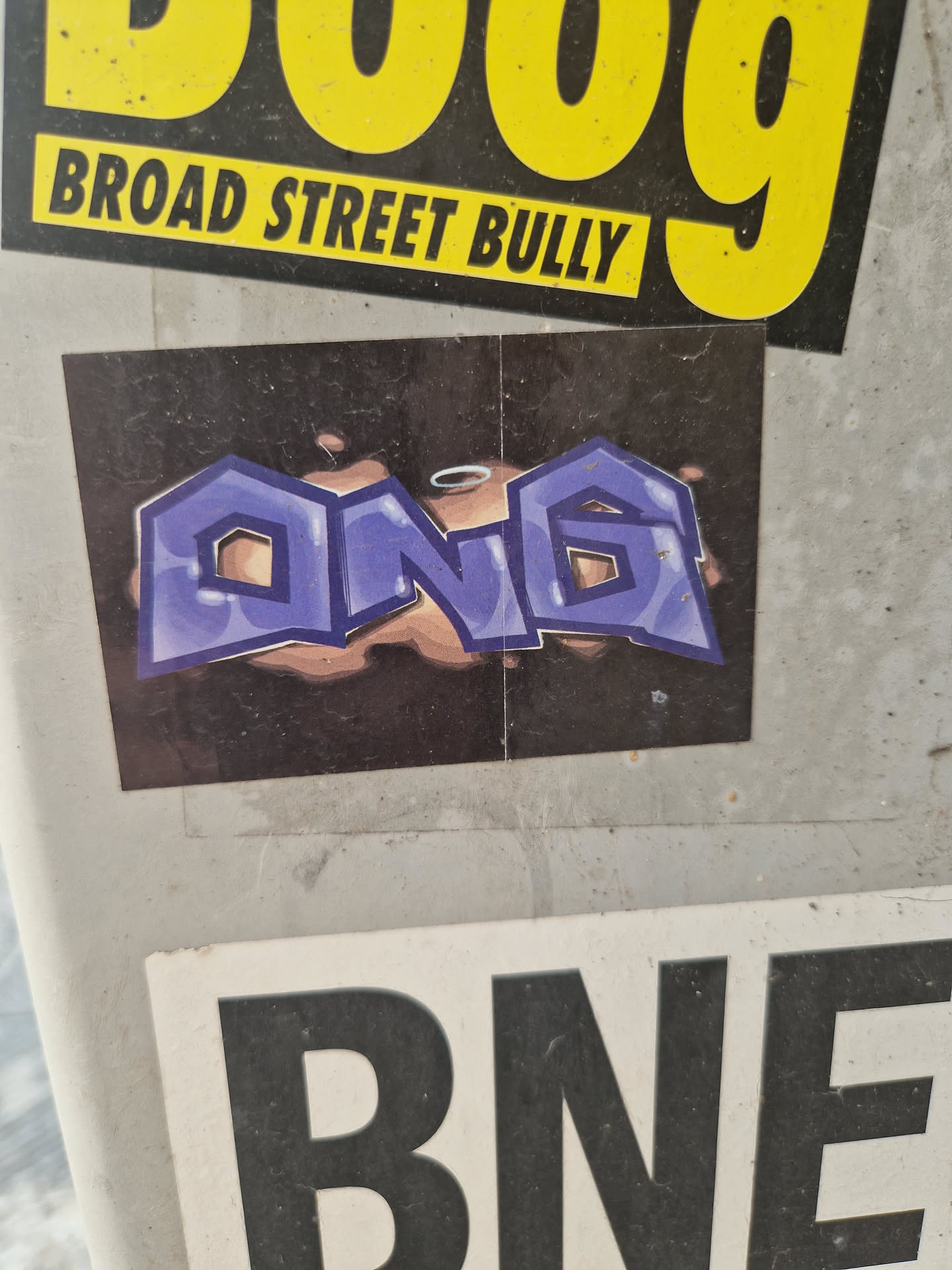 A sticker with graffiti-style lettering spelling 'ONG' in purple with a dark background. The letters have a bubbly, 3D effect.
