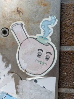 A sticker of a cartoon bong with a smiling face is stuck to a metal surface. The bong is light pink with a white outline. The face has closed eyes, thick eyebrows, and a small green smile. Steam is coming out of the top of the bong.