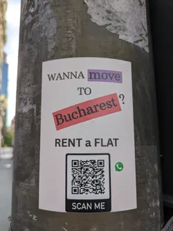 A sticker on a pole with the text "WANNA move TO Bucharest? RENT a FLAT". There is a QR code and a whatsapp icon below it.