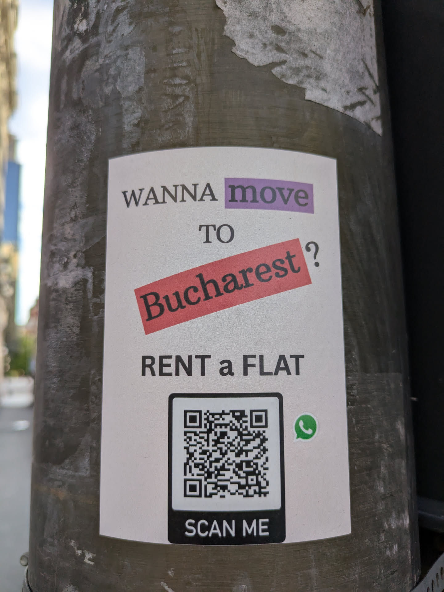 A sticker on a pole with the text "WANNA move TO Bucharest? RENT a FLAT". There is a QR code and a whatsapp icon below it.