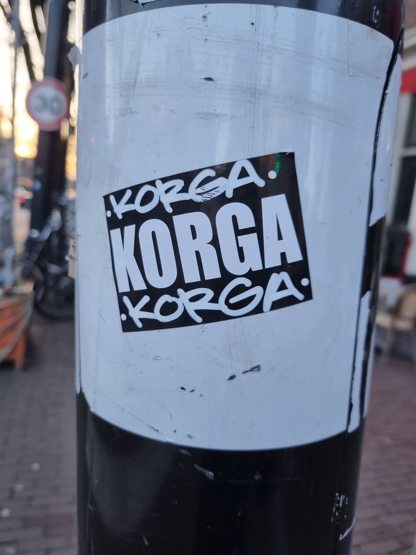 A worn-out sticker with the word KOPГA repeated three times, twice in a smaller, more stylized font and once larger and bolder in the center. The sticker shows some signs of wear and tear, indicating it has been exposed to the elements for a while.