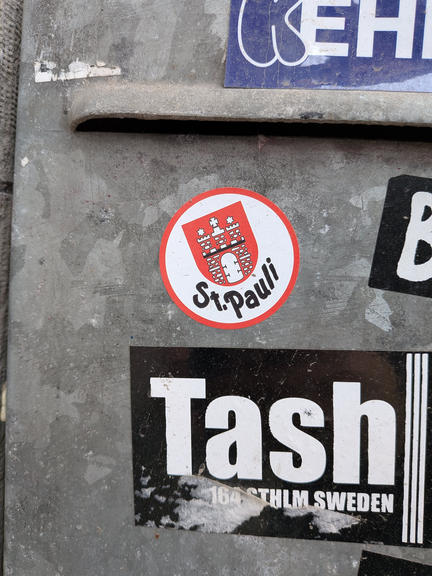 A circular sticker featuring a bold red outer border and a clean white background. The upper half displays a red shield containing a white depiction of a castle with three towers, a central gate, and a star positioned above the middle tower. Below this emblematic crest, the words "St. Pauli" are written in a distinctive, flowing black script.