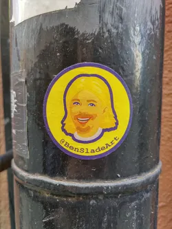 This circular sticker showcases a vibrant illustration of a person, possibly a self-portrait of the artist. The style is simple yet expressive, with bold colors and clean lines. The artist's social media handle is included in the design.