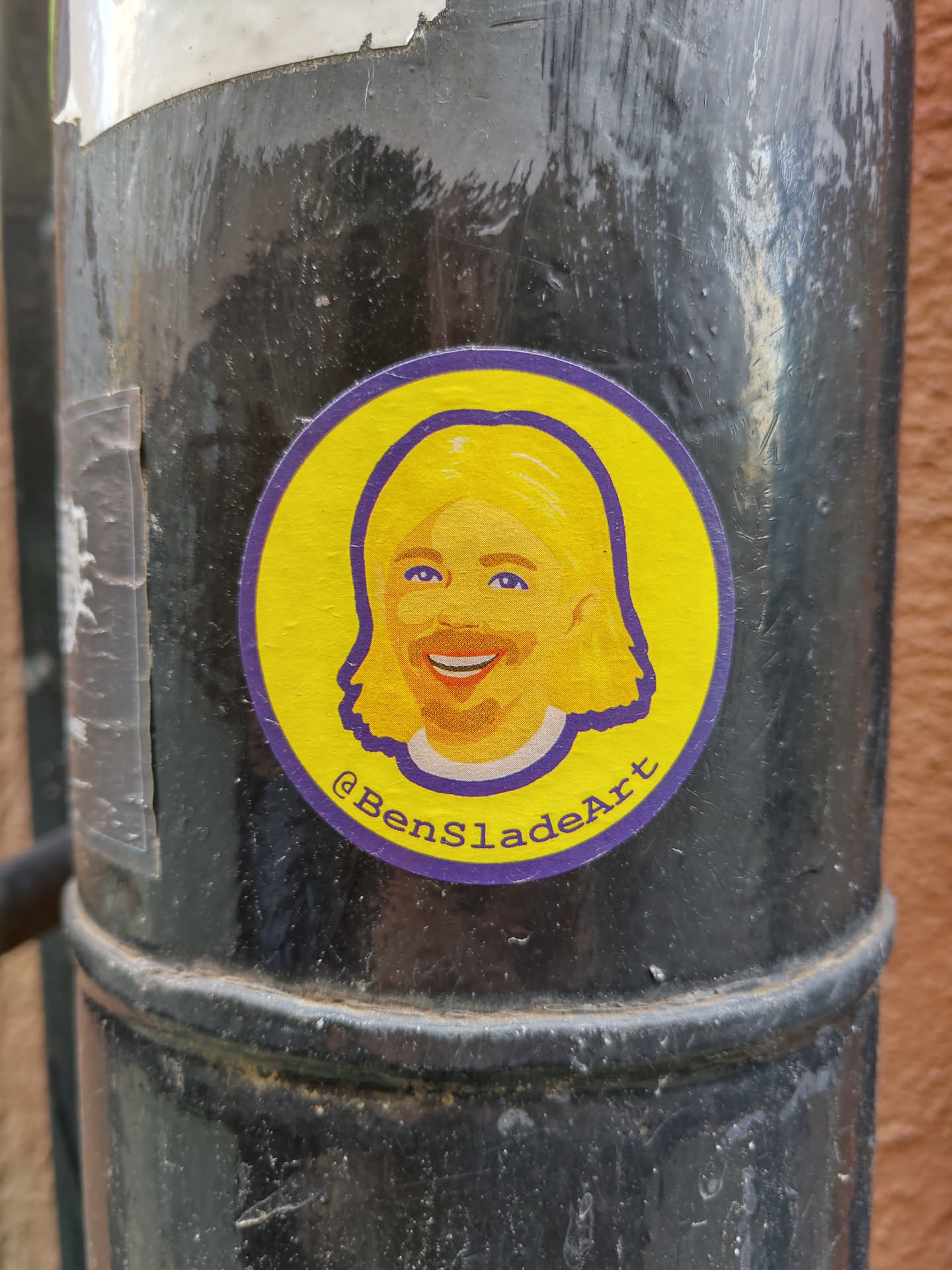 This circular sticker showcases a vibrant illustration of a person, possibly a self-portrait of the artist. The style is simple yet expressive, with bold colors and clean lines. The artist's social media handle is included in the design.