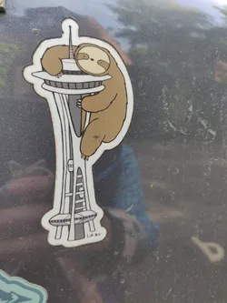 A sticker featuring a sloth hugging the Space Needle in Seattle.  The style is simple and cute.