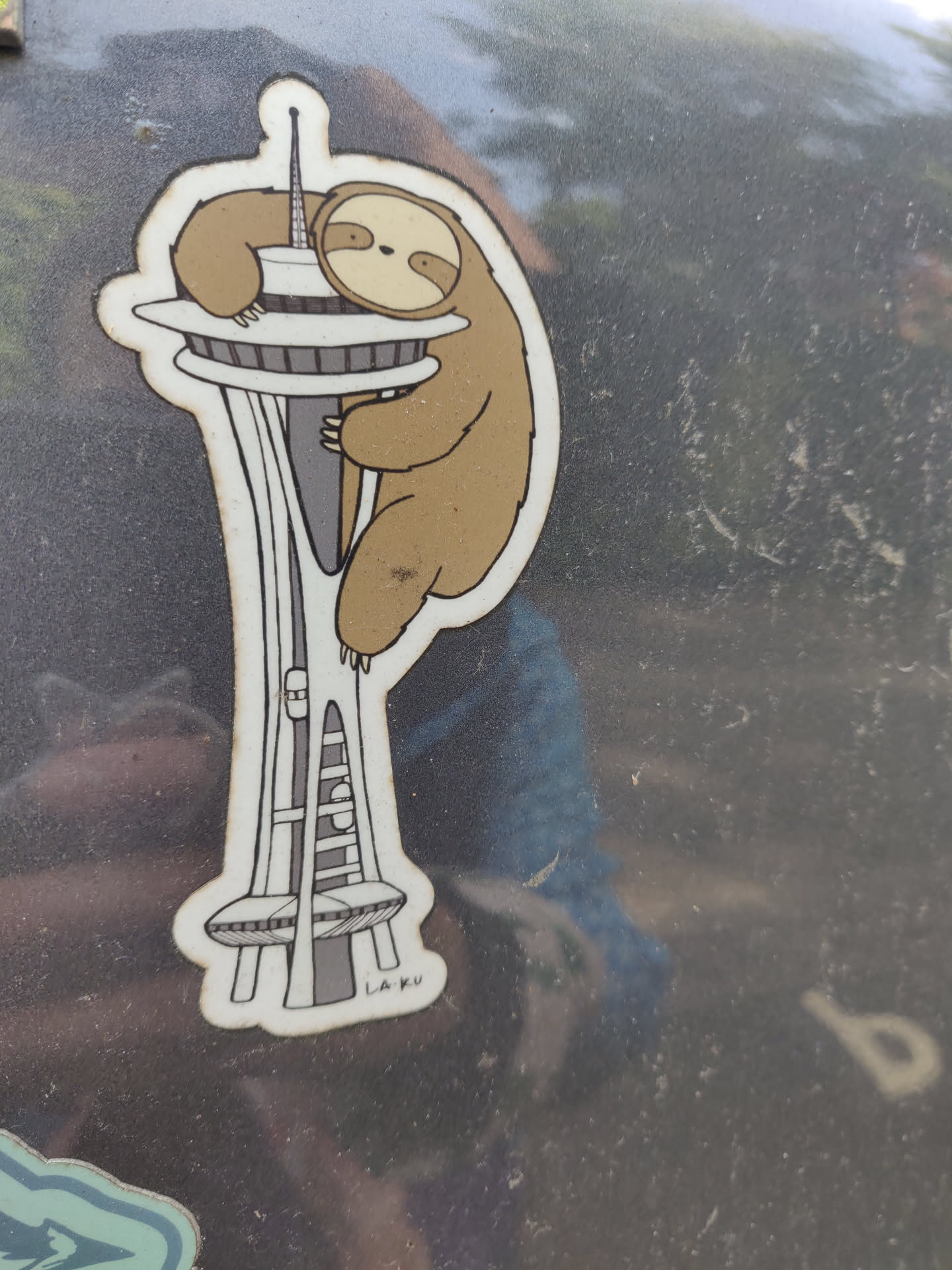 A sticker featuring a sloth hugging the Space Needle in Seattle.  The style is simple and cute.