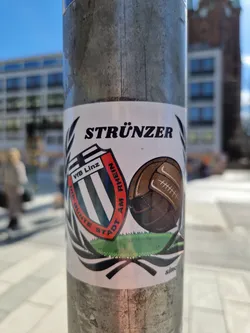 A sticker featuring the logo of VfB Linz, a football club from Linz, Austria. The sticker also includes the word "Strünzer" and an illustration of a vintage football.