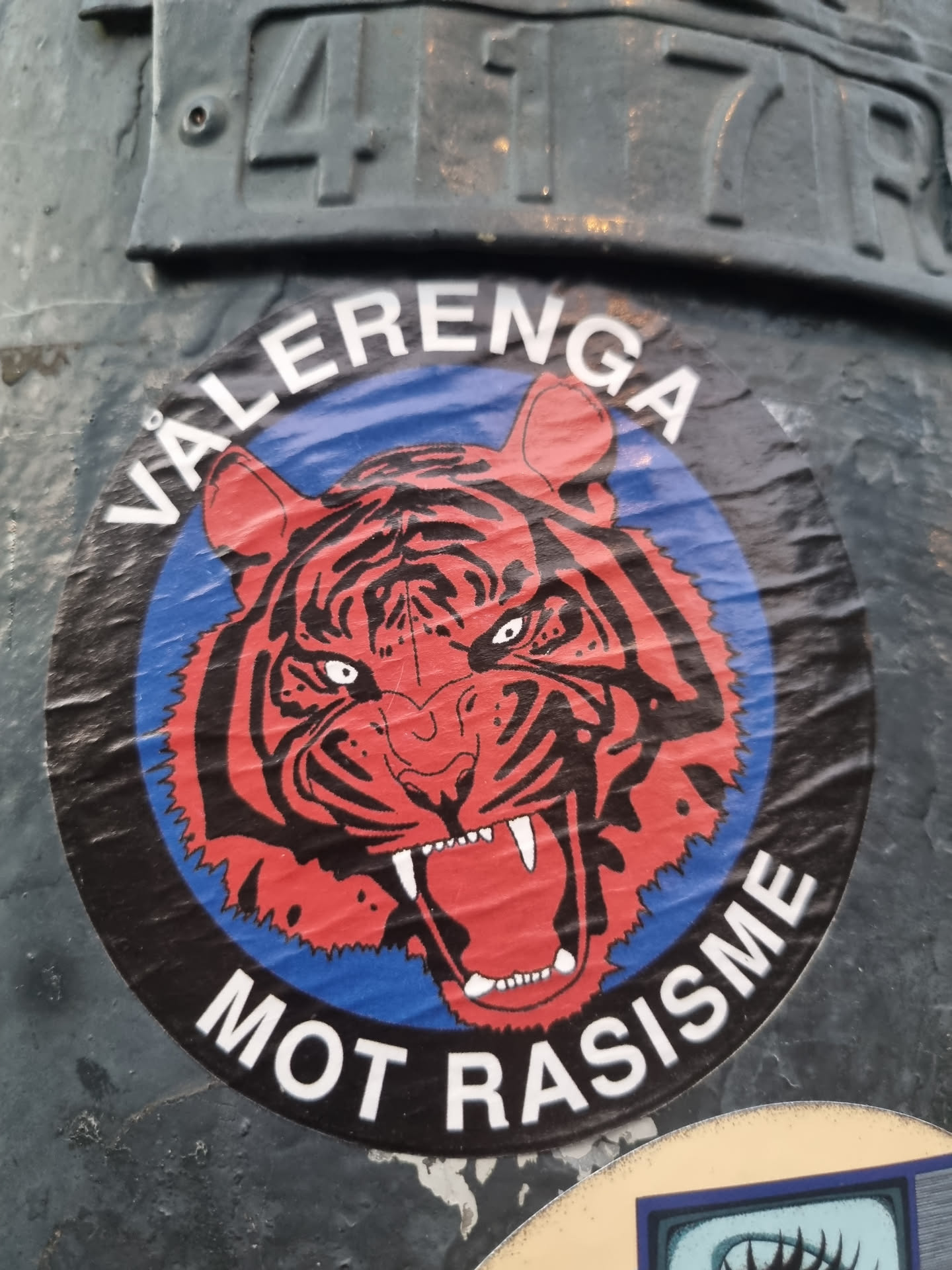 A round sticker with a tiger illustration in the center. The words "VALERENGÅ" and "MOT RASISME" are written around the tiger.
