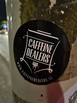 A black and white sticker with the text "Caffeine Dealers" in a stylized font.  The website www.caffeinedalers.nl is also printed on the sticker.