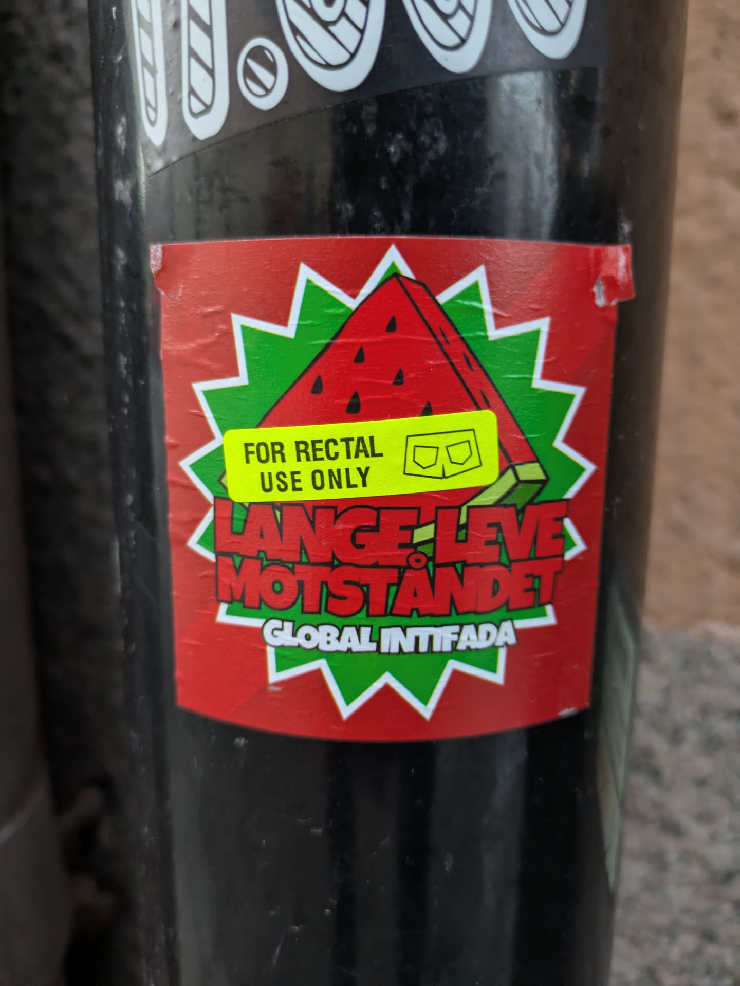 A red and green sticker with a watermelon illustration and the text "For rectal use only" on a yellow label.  The main text says "Länge Leve Motståndet" which translates from Swedish to "Long Live the Resistance" and the bottom reads "Global Intifada".