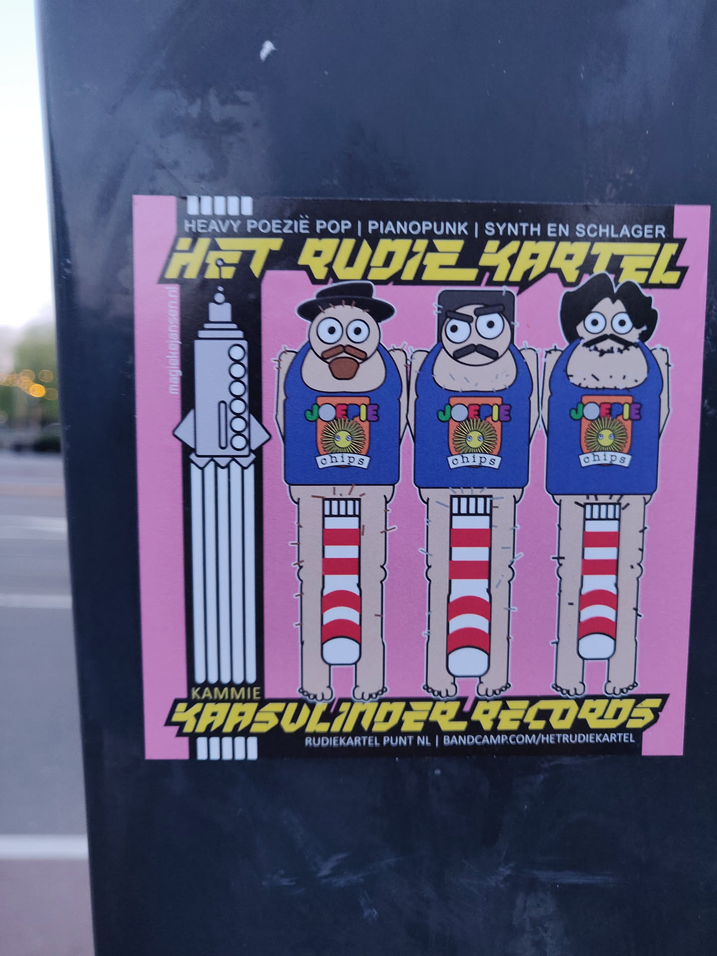 Sticker featuring three cartoon characters with the text Het Rudiekartel, Kammie Kaasulinder Records, and bandcamp.com/hetrudjekartel.  The sticker also includes the text Heavy Poezie Pop | Pianopunk | Synth en Schlager.