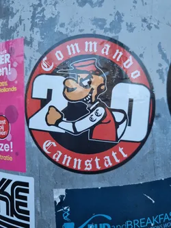 A round sticker featuring a cartoon character resembling Popeye, the number 20, and the text 'Commando' and 'Cannstatt' in a Gothic style font. The character is depicted in a red and black uniform.