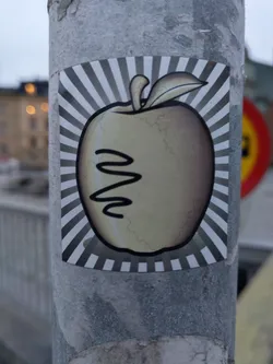 This sticker features a stylized illustration of an apple against a sunburst background.  The apple appears slightly weathered or distressed, adding to its unique charm.  There is a simple design on the apple that resembles a squiggly line or a face. 