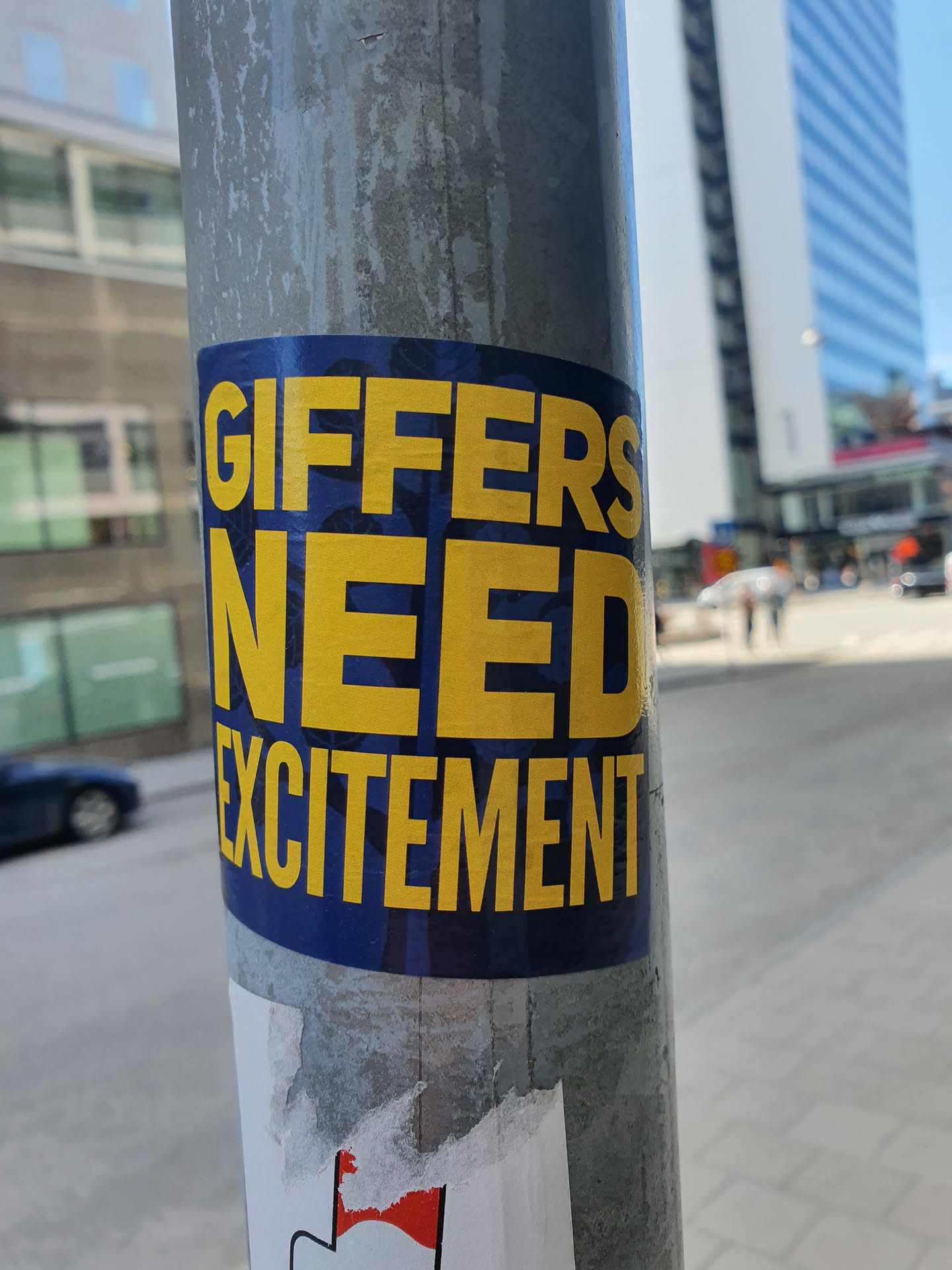 A blue and yellow sticker on a pole with the text "Giffers need excitement!"
