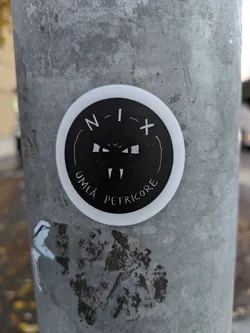 Round sticker with a black and white illustration and text. The text says N-I-X in the upper part of the circle and Umeå Petricore in the lower part. There is a small drawing between the texts.