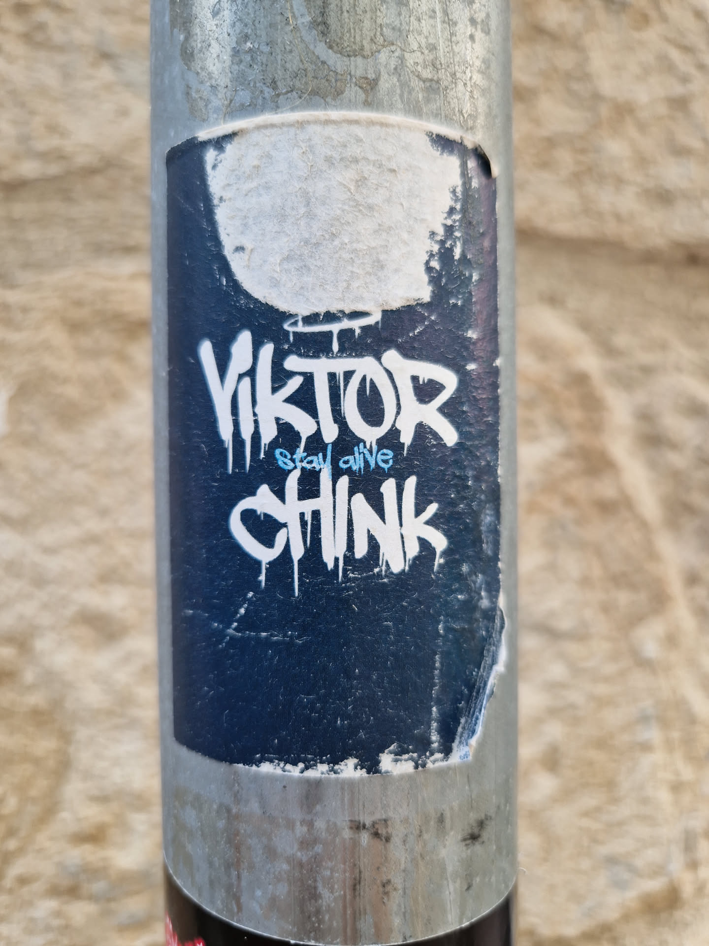 A dark blue sticker with white graffiti-style text. The text says "Viktor" over "Stay alive" over "Chink". The sticker is slightly damaged and peeling at the edges.