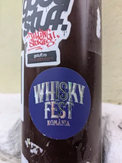 A circular sticker with a blue background. The text "WHISKY FEST" is displayed in a holographic, stylized font. Below that, "ROMANIA" is written in smaller, similar font.