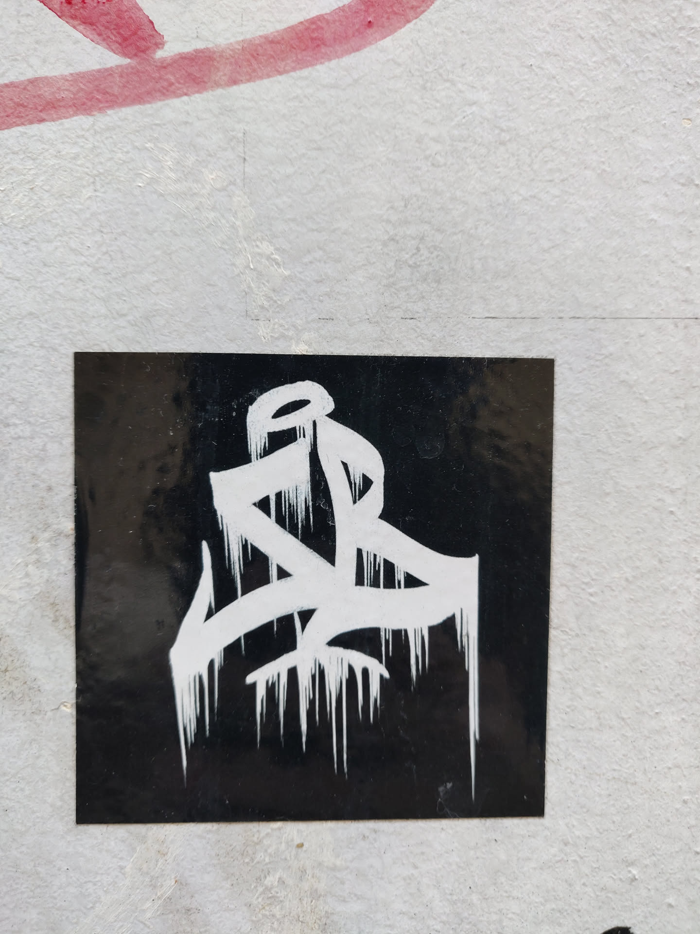 A black square sticker with white abstract graffiti art. The style is dripping, suggesting movement and energy. The contrast is striking and the design is bold.