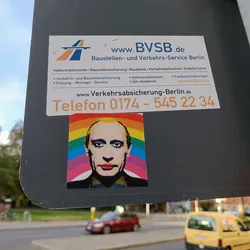 A sticker featuring Vladimir Putin's face superimposed on a rainbow background. The sticker is affixed to a larger sign advertising Baustellen- und Verkehrs-Service Berlin.