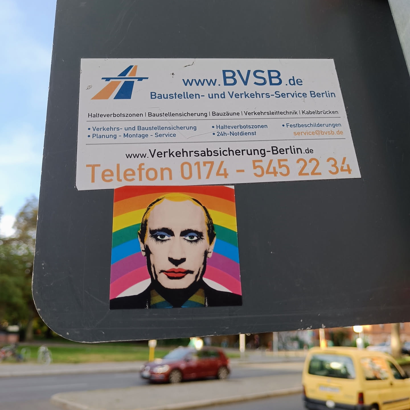 A sticker featuring Vladimir Putin's face superimposed on a rainbow background. The sticker is affixed to a larger sign advertising Baustellen- und Verkehrs-Service Berlin.