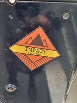 Orange and yellow diamond shaped sticker with a mountain range graphic and the text 'IMPACT' over 'Boulderhal'.