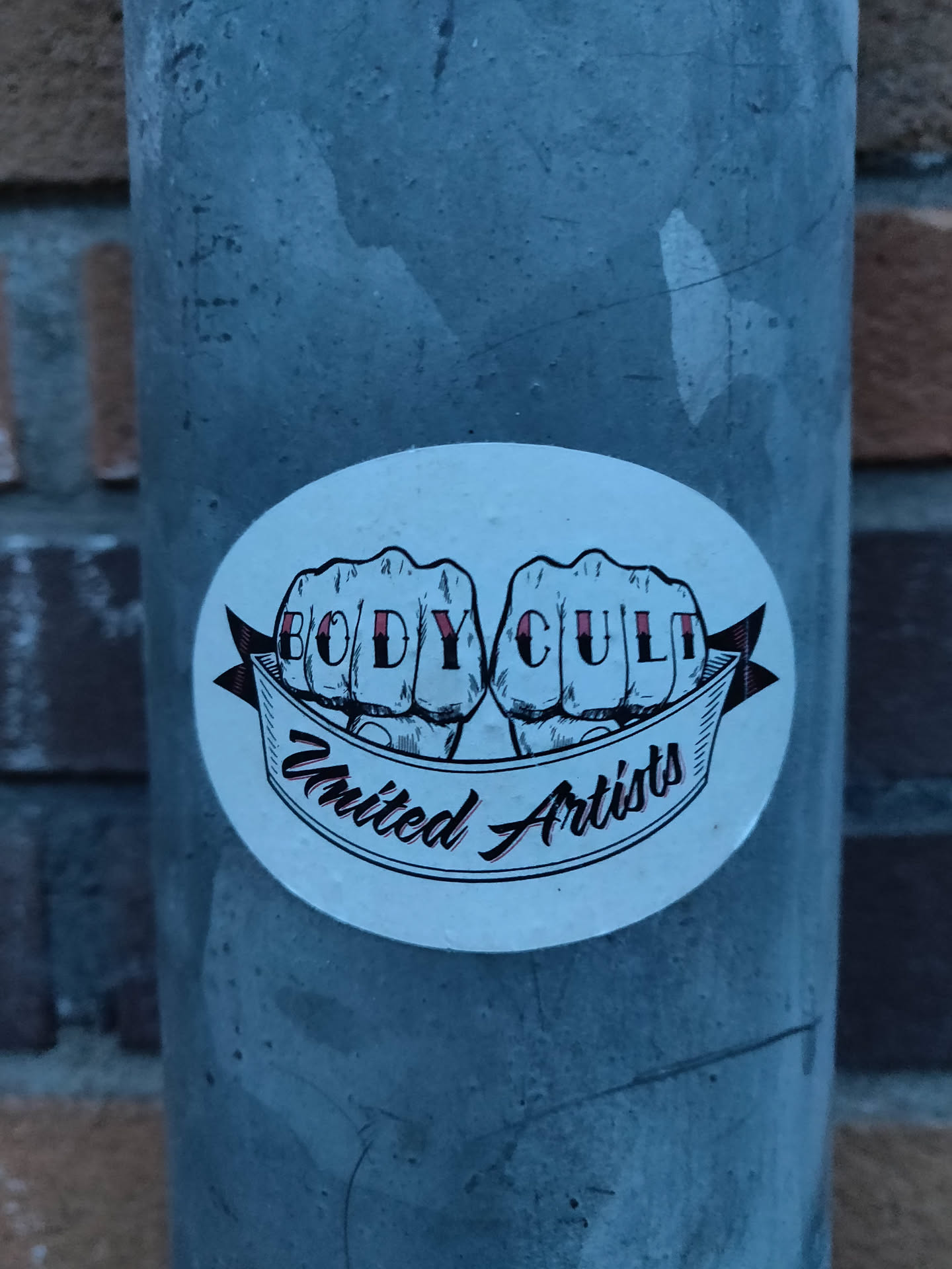 A round sticker featuring two fists with the words BODY CULT in between them, and the words "United Artists" on a banner below. The design is in black and white with a hint of red.