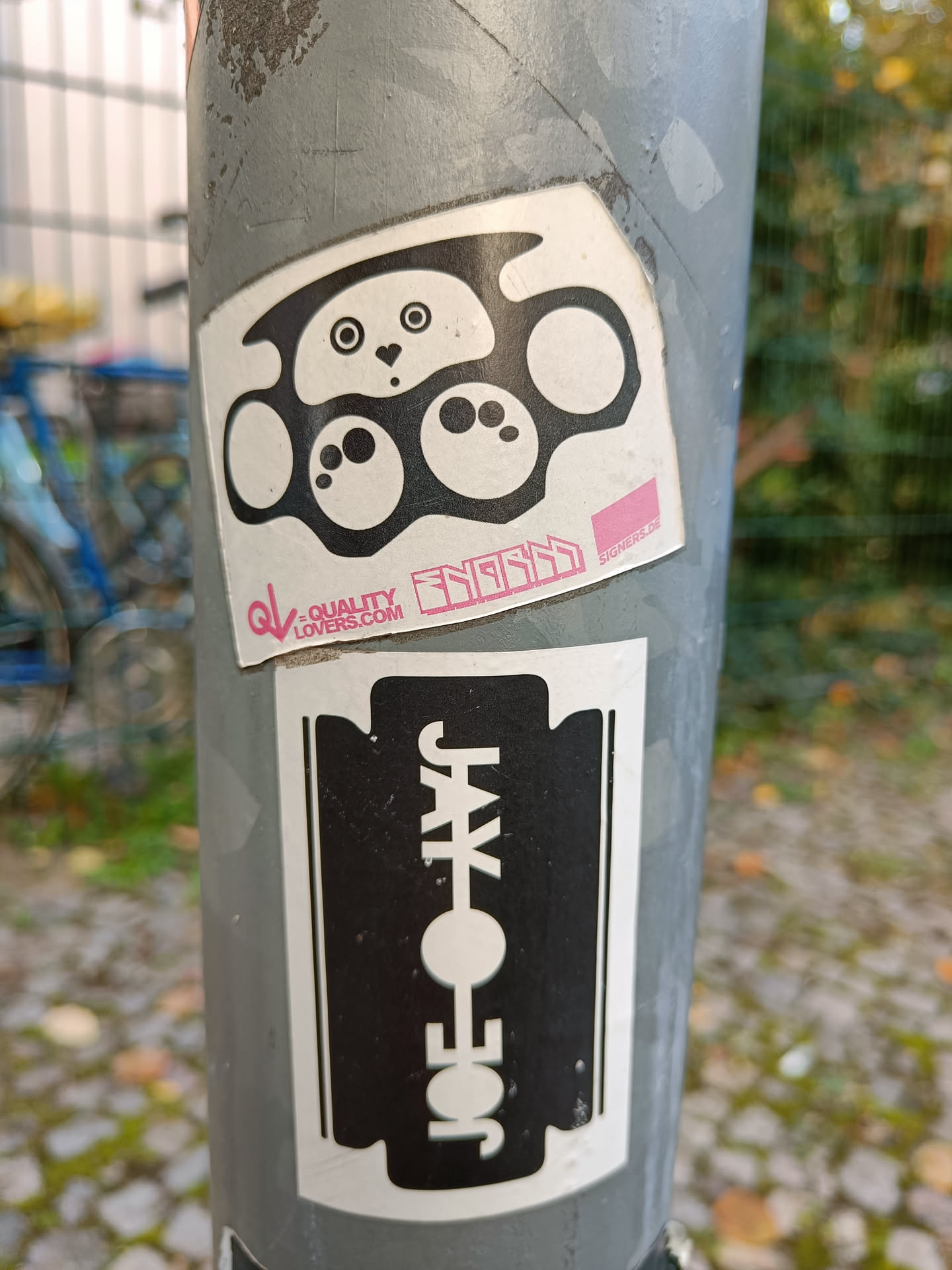 A black and white sticker featuring a cute panda face incorporated into a brass knuckles design.  The sticker also has some text that says "SNUGGLE" and a website address, qualitylovers.com. Below it is another sticker of a razor blade with "JOE JAY" written on it. 