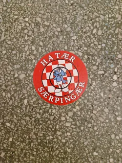 Round red sticker with a checkerboard pattern and a smurf-like character in the center. The text "HATER" is written at the top and "SERPINGAER" at the bottom of the circle. 