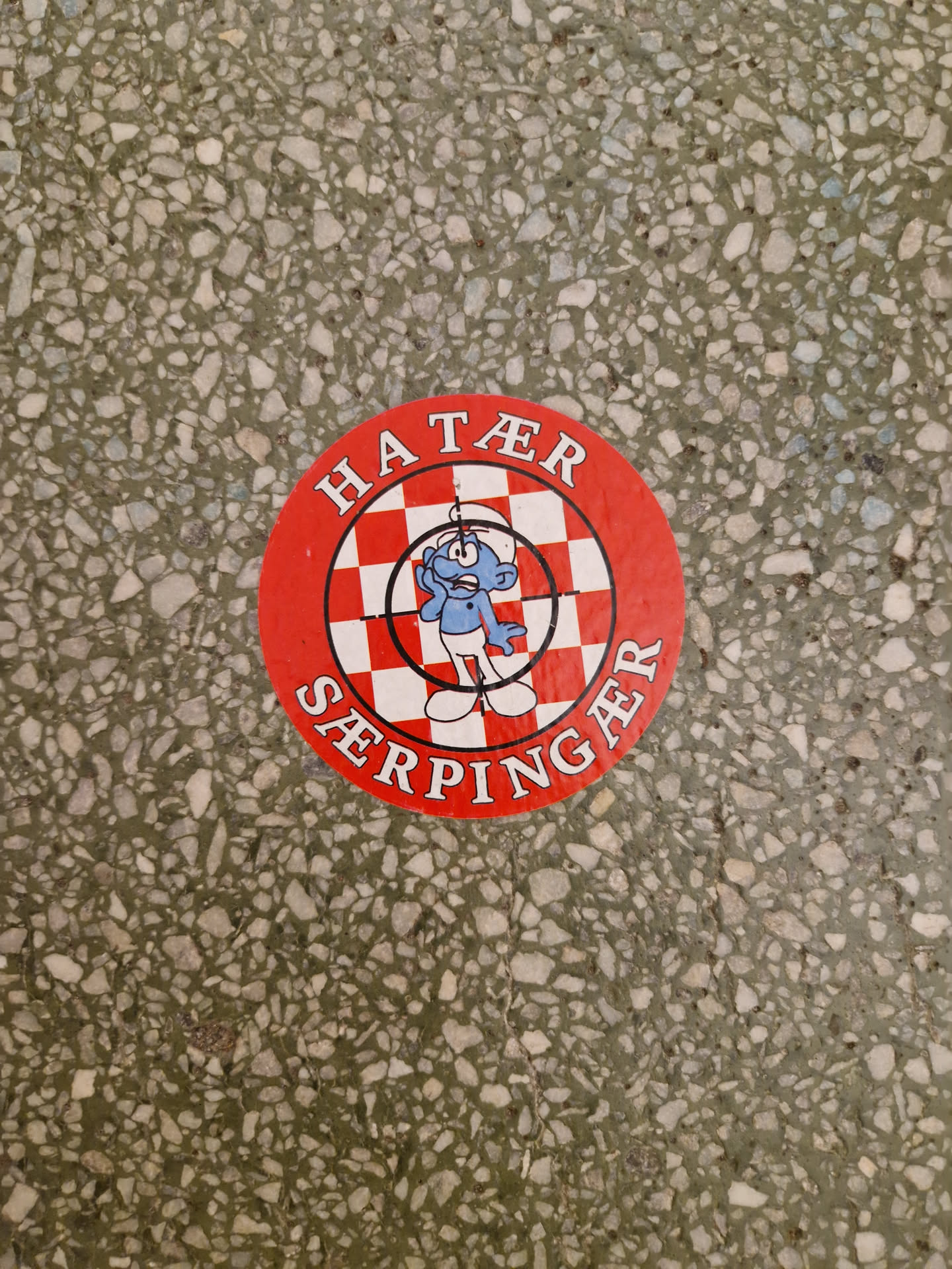 Round red sticker with a checkerboard pattern and a smurf-like character in the center. The text "HATER" is written at the top and "SERPINGAER" at the bottom of the circle. 